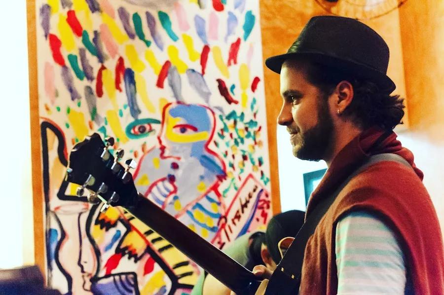 Perfil e violão diante de um mural de rostos.